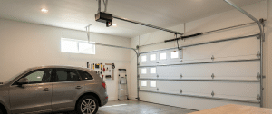 A clean, organized garage with a silver SUV parked inside, a white garage door, tool racks on the wall, a ladder, and a window letting in natural light.