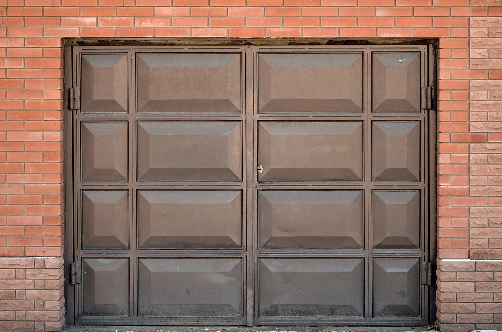 The texture of a painted metal gate from a brick garage. Large metal doors built into the wall of old brick