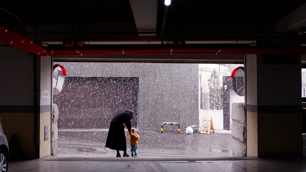 	
An adult and a child stand at the entrance of a garage door in Parker, watching as snow falls heavily on the street outside.