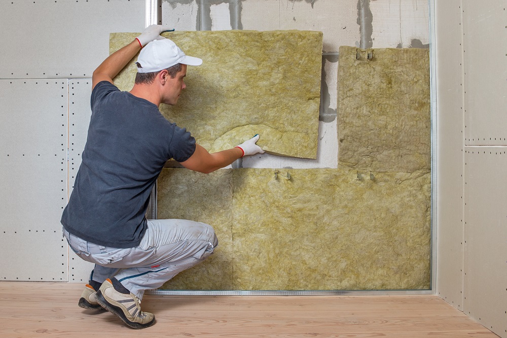  A man wearing gloves installs insulation panels into a wall frame during a construction or renovation project, demonstrating techniques used when selecting the best insulation for garage doors.