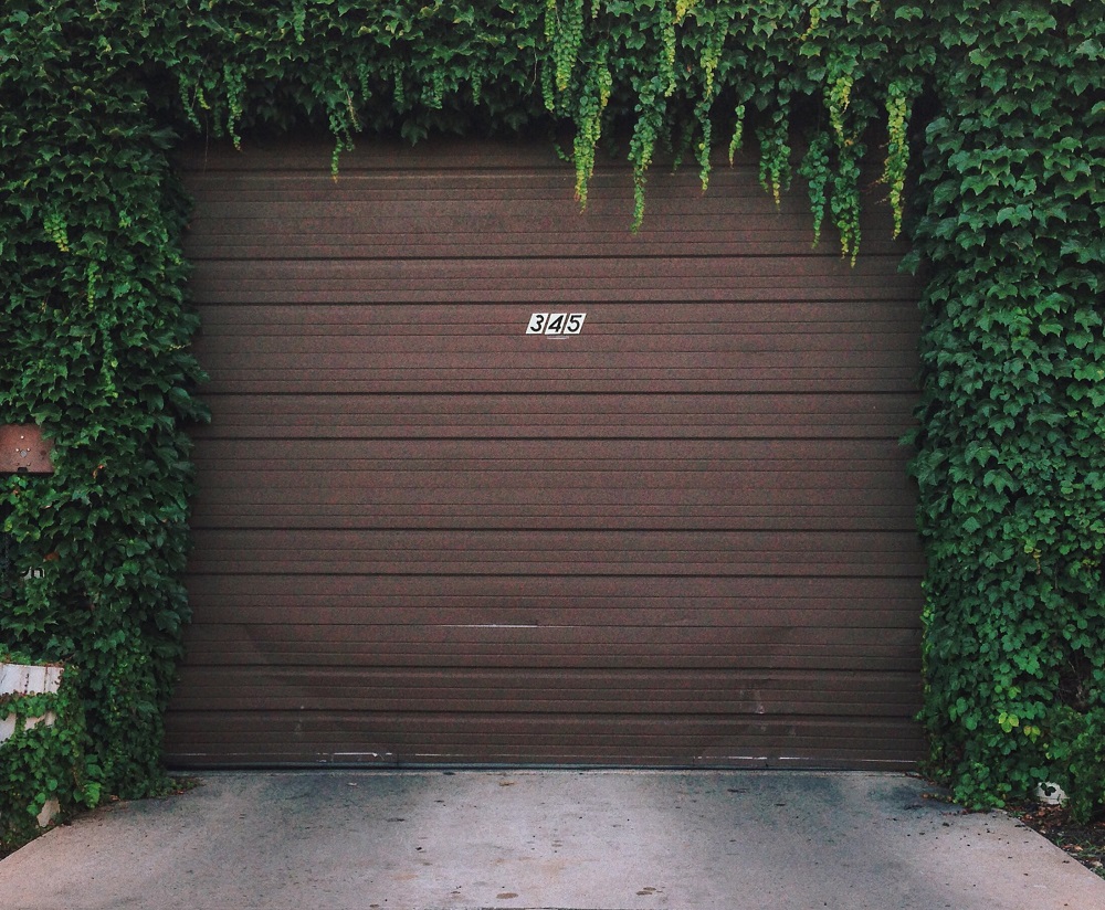 A brown garage door with the number 345 is surrounded by green ivy covering the top and sides, offering a picturesque view for those seeking Same-Day Garage Door Service Lakewood.