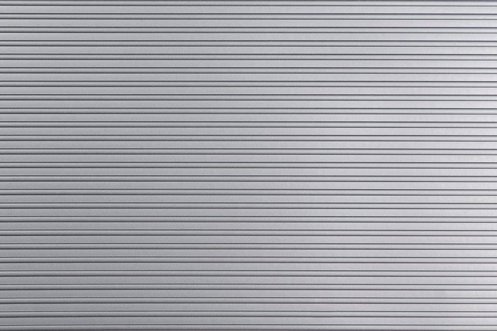 Close-up view of a silver metallic surface with evenly spaced horizontal grooves running across the entire image, resembling patterns left by hailstorms in Parker.