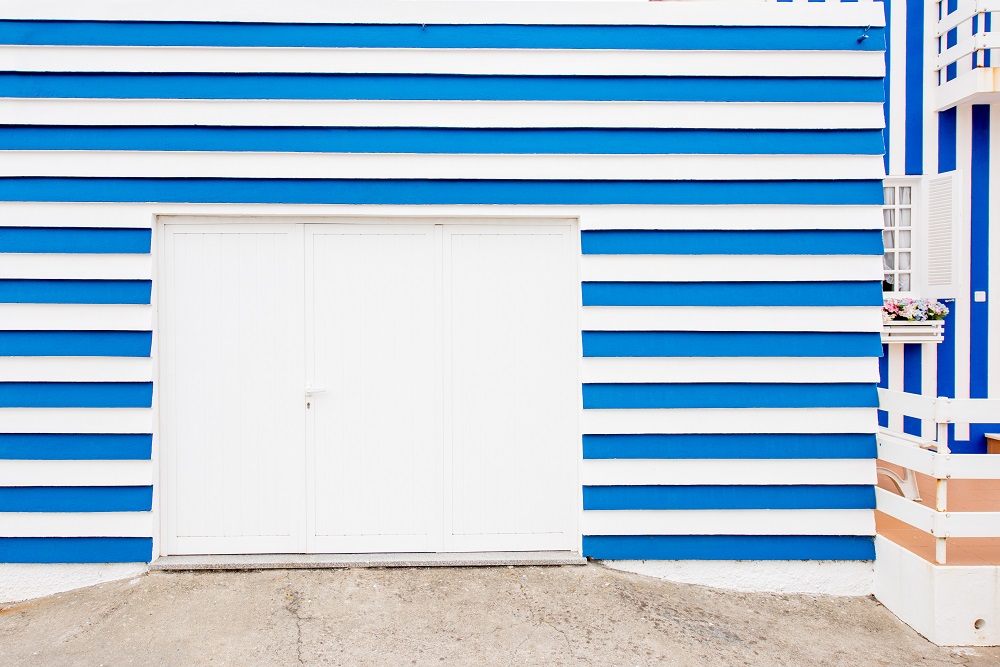 White Garage door in a building exterior with bright blue and white horizontal stripes, following HOA Rules for Garage Door in Lakewood. A small window and flower box are visible on the right side.