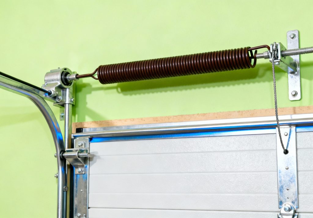 Close-up of a metal torsion spring mechanism installed above a white sectional garage door against a light green wall, ideal for showcasing garage door spring repair Parker services.