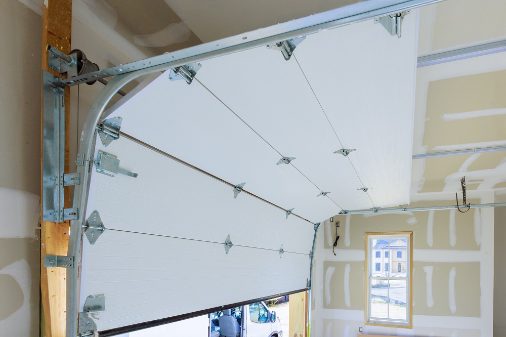 An automatic garage door is partially open inside a residential garage with unfinished drywall and a small window letting in daylight, highlighting the importance of regular Garage Door Maintenance Parker homeowners can trust.