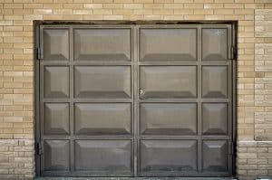 A closed, rectangular, brown garage door set in a brick wall shows a small dent and some discoloration.