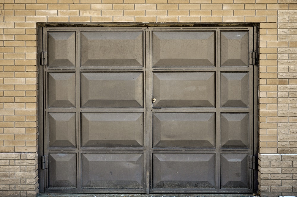  A closed, rectangular, brown garage door set in a brick wall shows a small dent and some discoloration—features that may not comply with HOA Rules for Garage Door in Lakewood.