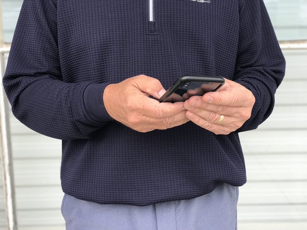 A person wearing a dark long-sleeve shirt and a gold ring holds and uses a smartphone with both hands.