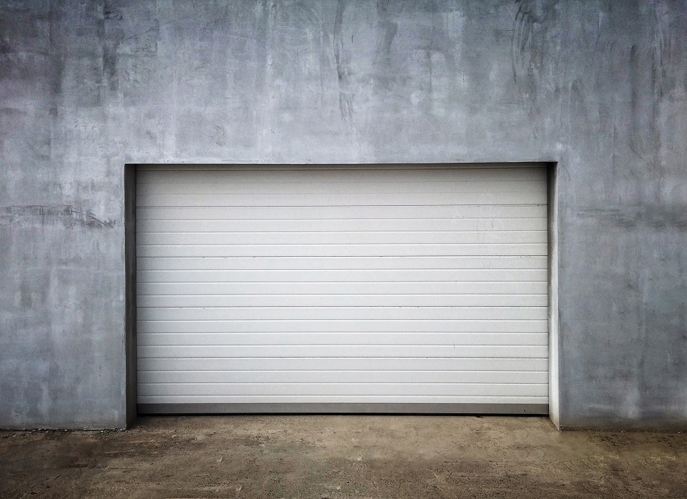 	
Modern gray house exterior with a large garage door—ideal for replacing just one panel of a garage door—plus a paved driveway and green shrubs along the side.