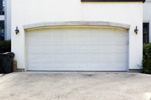 A closed white garage door on a residential building, with outdoor wall lamps on each side and trash bins to the left—an ideal setting for a Garage Door Replacement in Greenwood.