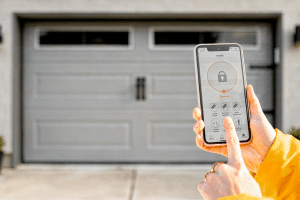 A person uses a smartphone app to control or monitor garage doors Lakewood in front of a house.
