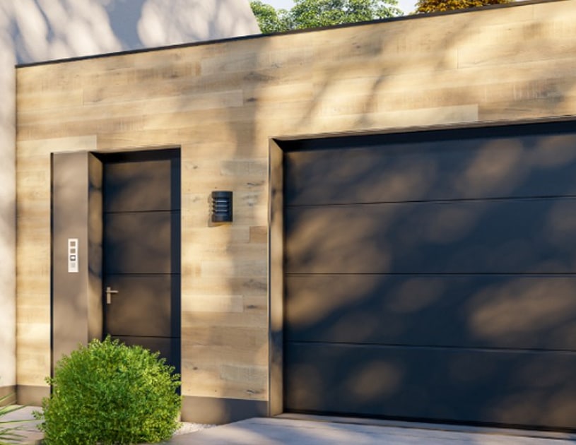Modern house exterior with light wood siding, flush dark door on the left, and large matching garage door on the right. Need Garage Door Repair in Lakewood, CO? Green bush in the foreground completes the contemporary look.