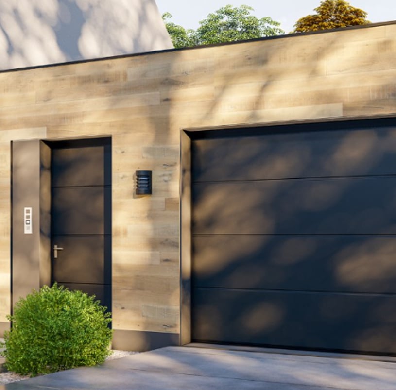 Modern house facade with a wood-paneled exterior, black garage door from a Commercial Garage Door Installation in Lakewood, CO, sleek black entry door, wall light fixture, and a small green shrub in front.