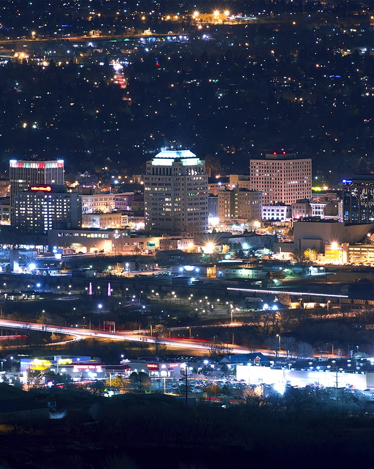 A cityscape at night with illuminated buildings, streetlights, and traffic, viewed from an elevated vantage point.
