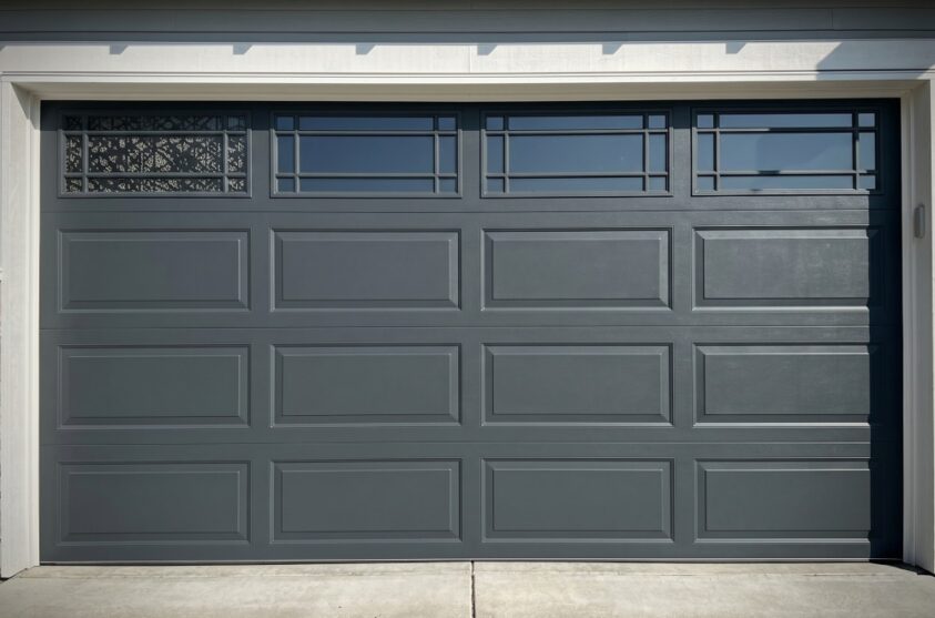 A closed dark gray garage door with rectangular panels and a row of small windows at the top.