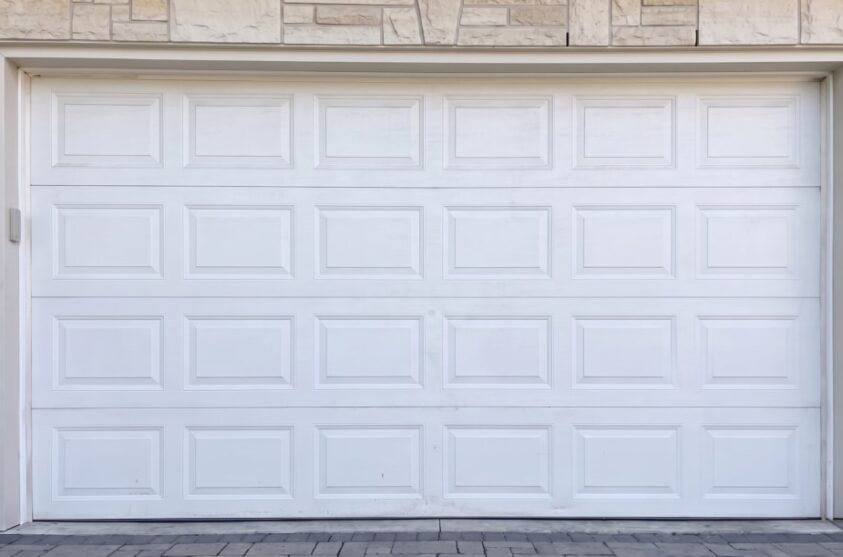 A white garage door in a residential area before the renovation