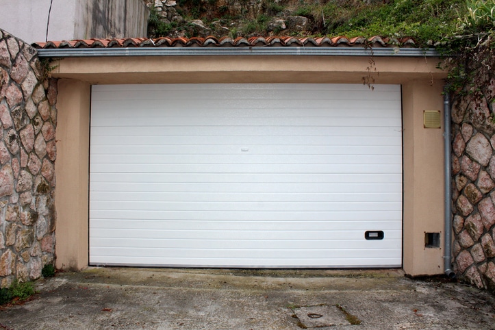 A closed white garage door set in a stone and stucco wall with a tiled roof, on a concrete driveway.