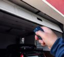 A person uses a remote control to open a white garage door, revealing a parked car inside the garage.