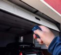A person uses a remote control to open a garage door, with a car parked inside the garage.