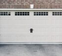 Closed beige garage door with rectangular panels and three small windows at the top, set in a brick and stone exterior wall.