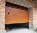 Partially open wooden garage door in a brick building under construction, with tools and materials visible inside the garage.