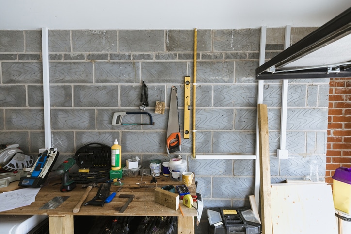 A workbench in a garage with various tools, glue, paint cans, and a spirit level on a brick wall.