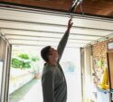 A man inside a garage reaches up to manually open or close a partially raised garage door.