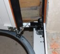 Close-up of a garage door mechanism showing the metal track, cable, hinge, and part of the unfinished wall with exposed bricks.