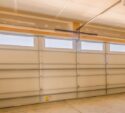 Interior view of a clean, empty garage with a closed sectional garage door featuring four rectangular windows near the top.
