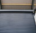 A metal roller shutter door is partially open inside an industrial building with a corrugated roof and metal frame.