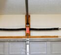 A broken, loose garage door torsion spring mounted above a closed gray garage door inside a garage.