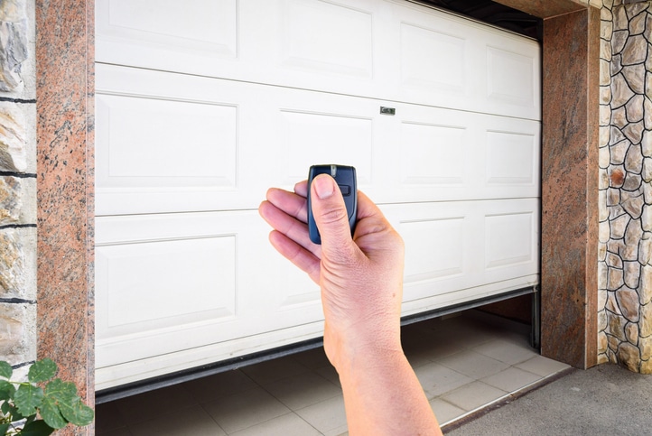 A hand holding a remote control in front of a partially open white garage door.