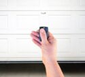 A hand holding a remote control in front of a closed white garage door.