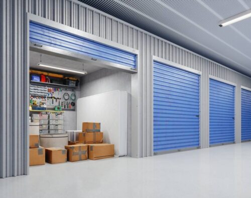 A row of storage units with blue doors; one unit is open, revealing cardboard boxes, a mattress, and organized tools hanging on the back wall.