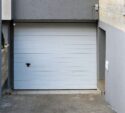 Closed white garage door set in a recessed concrete driveway, surrounded by gray and beige walls.