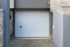 Closed white garage door set in a recessed concrete driveway, surrounded by gray and beige walls.