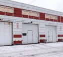 A row of industrial garage doors in a building with red and white panels, one door showing a green light, others red, with snow on the ground.