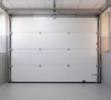 Closed white sectional garage door viewed from inside a clean, modern garage with tiled floor and gray walls.