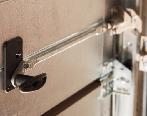 Close-up of a metal garage door lock mechanism with a handle and sliding bolt in the locked position.