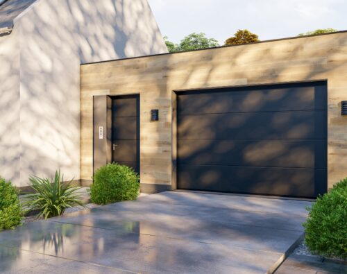 Modern house exterior with a light wood-paneled garage, black garage door, black side door, outdoor lights, and neatly trimmed shrubs along a paved driveway.