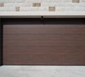 Closed brown garage door with horizontal panels set in a light-colored brick wall with a small exterior light above the door.