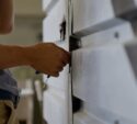 A person uses a tool to unlock or repair a metallic rolling shutter door.