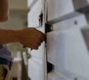 A person uses a tool to unlock or repair a large metal industrial door or panel.