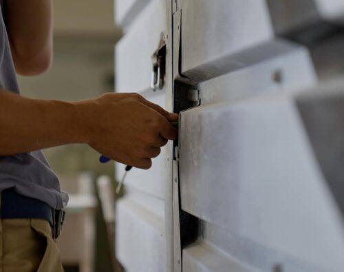 Person unlocking or locking a large metal door with a key, only their torso and hands visible.