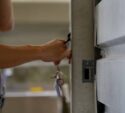 A person holds a set of keys and unlocks a metal door or cabinet with one hand.