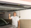 Man closing door in a garage with remote control, standing beside his car