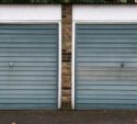 Two closed blue-grey garage doors set in a brick wall with white trim, viewed from the street.