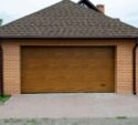 A closed wooden garage door set in a brick-walled garage with a paved driveway in front.