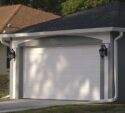 A closed white garage door on a suburban house with two black wall-mounted lanterns on either side.