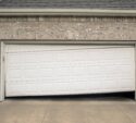 A white garage door is partially open and appears broken, sagging unevenly in the middle.
